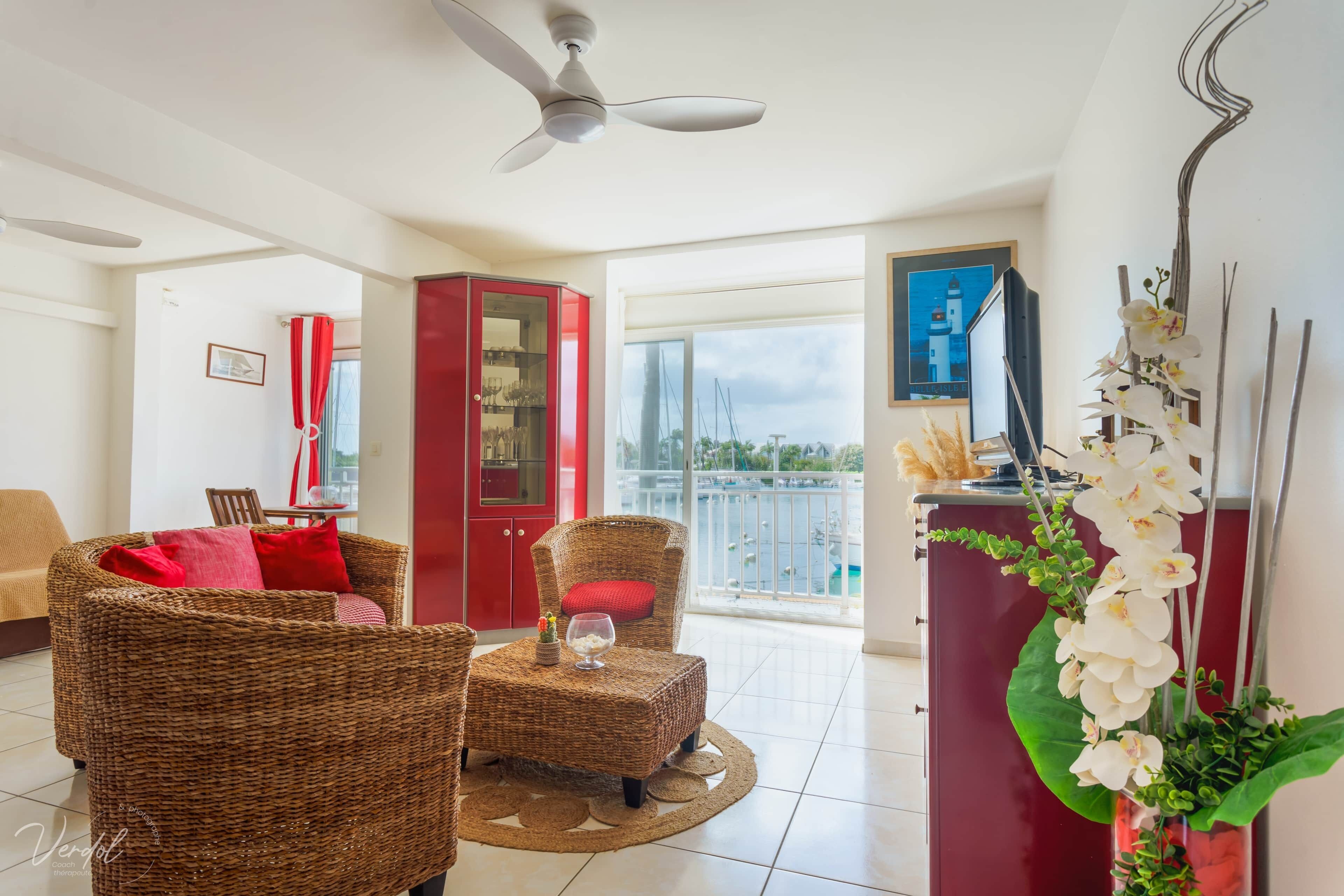 A spacious living area with wicker furniture, a red cabinet, and a balcony with a view.