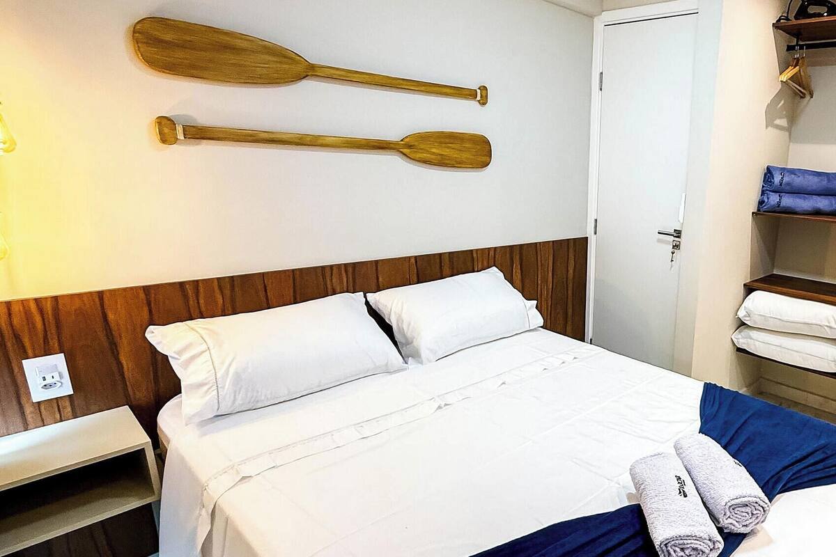 Une chambre d’hôtel avec un lit, une décoration murale en forme de pagaie en bois, une porte blanche et une serviette sur le lit.