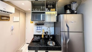 Ett kompakt kök med ett kylskåp i rostfritt stål, en inbyggd mikrovågsugn och en kaffebryggare.
