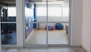Ένα γυμναστήριο με εξοπλισμό γυμναστικής, ένα μεγάλο παράθυρο και έναν μπλε τοίχο με μια τοιχογραφία.