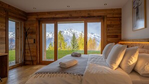Ein Schlafzimmer in einer Holzhütte mit einem Bett, Kissen und Blick auf schneebedeckte Berge.