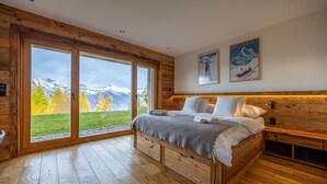 Ein schlafzimmer im Holzblockhausstil mit einem großen Bett, Holzdielen und Blick auf schneebedeckte Berge durch große Fenster.