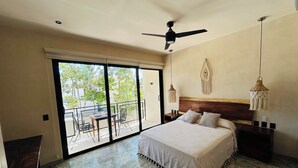 Une chambre avec un grand lit, un ventilateur de plafond, un balcon avec une table et des chaises, et une décoration murale en macramé.