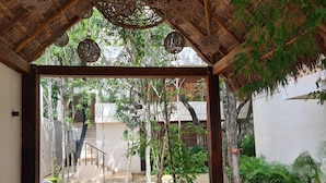 Un espace extérieur abrité, doté d’un chemin en pierre, d’une pergola en bois, de lampes en osier suspendues et d’une végétation luxuriante.