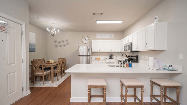 A modern kitchen with white cabinets, a central island with bar stools, a stainless steel refrigerator, and a clock on the wall. - Rebel Bluff on Depot by Apex Short Term Stays (Oxford)