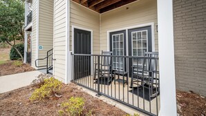 A two-story building with a covered porch, a small outdoor seating area, and a brick wall adjacent to the building. - Rebel Bluff on Depot by Apex Short Term Stays (Oxford)
