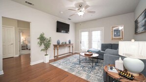 A living room with hardwood flooring, a ceiling fan, a grey sofa, a coffee table, a TV mounted on the wall, and a framed picture. - Rebel Bluff on Depot by Apex Short Term Stays (Oxford)