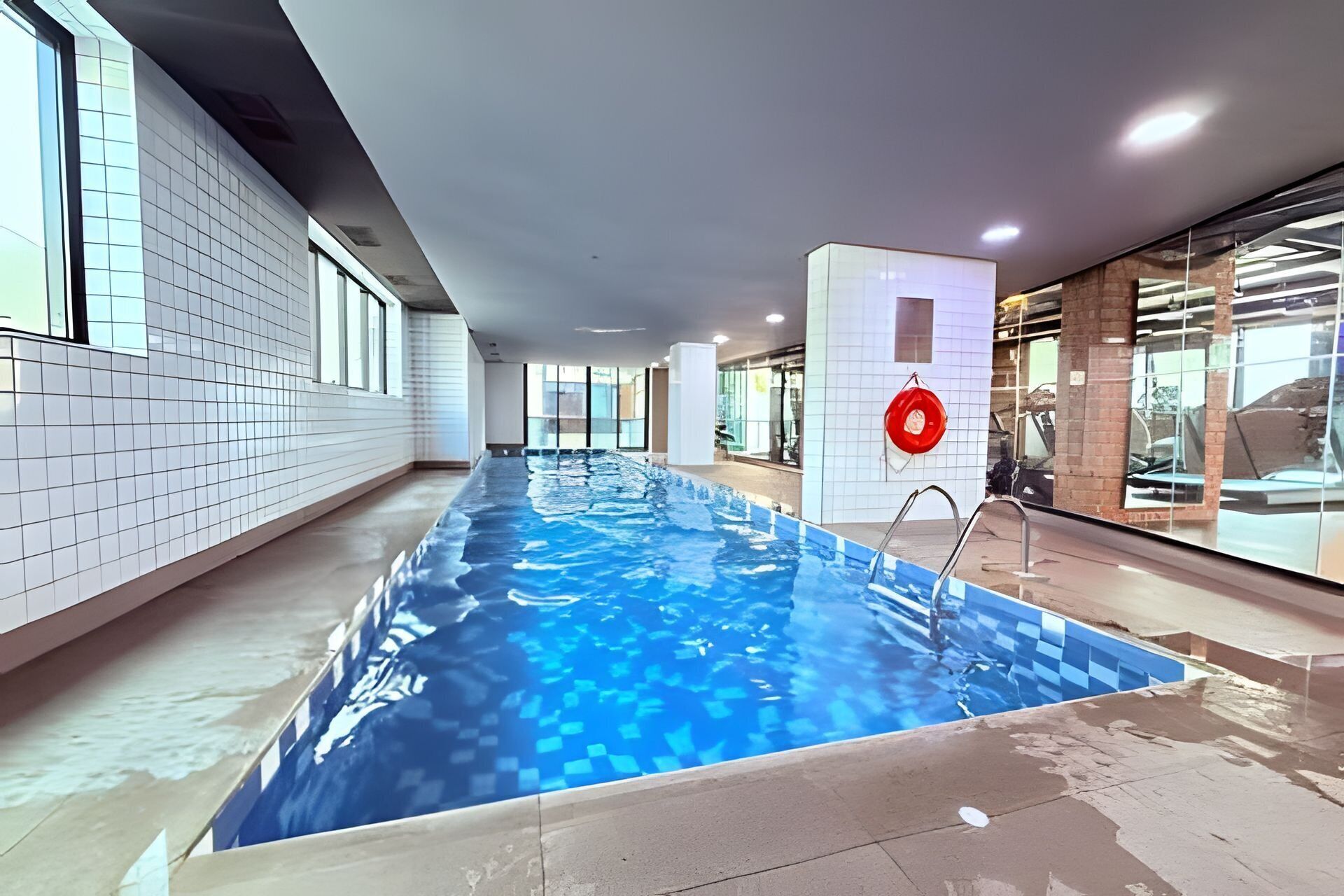 An indoor swimming pool with clear blue water, surrounded by tiled walls and windows.