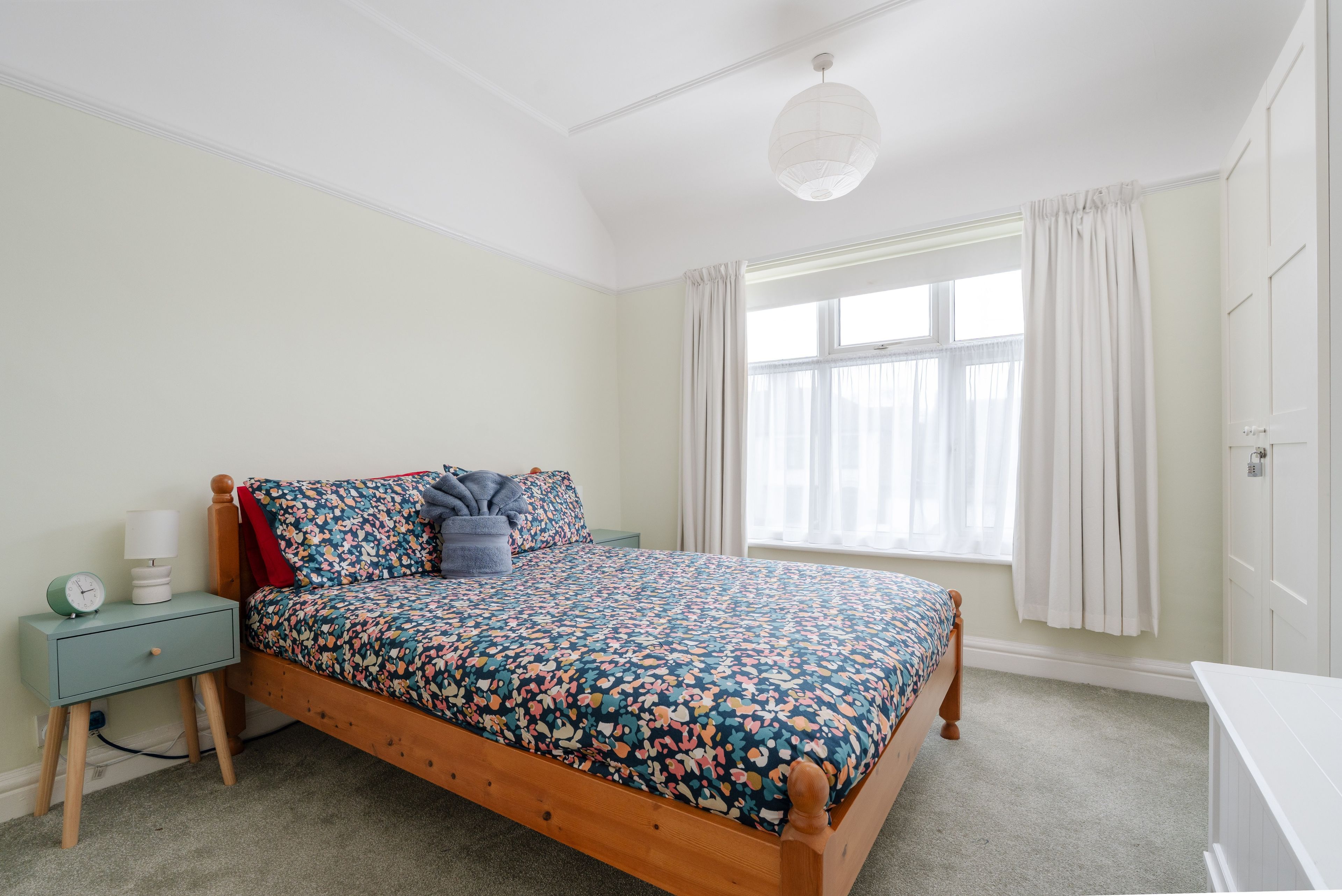 Une chambre à coucher avec un lit en bois, une table de chevet, une lampe et une fenêtre avec des rideaux.