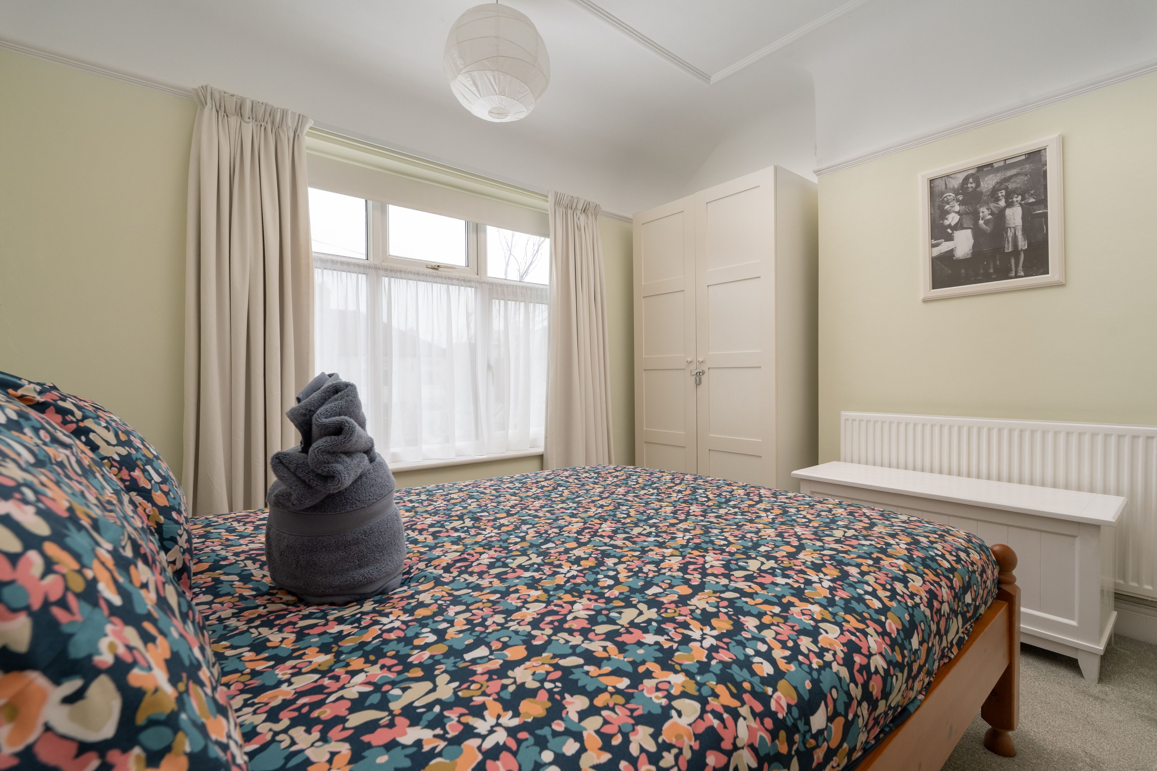 Ein Schlafzimmer mit einem Bett, einer Bank, einem Heizkörper und einem Fenster mit Vorhängen.
