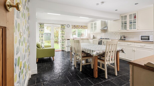 A kitchen with a dining table and chairs, a green armchair, and a view of the garden through the door. - Music Lovers | Piano | Pets OK & Driveway Parking (Liverpool)