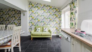 A kitchen with a green sofa, a dining table with chairs, a dishwasher, and a window with a curtain. - Music Lovers | Piano | Pets OK & Driveway Parking (Liverpool)