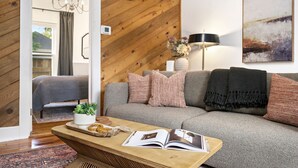 Un salon chaleureux avec un canapé gris, une table basse en bois sur laquelle sont posés un livre et des objets décoratifs, une lampe et un tableau au mur.