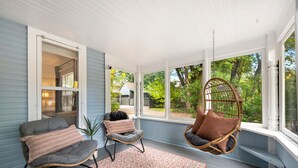 Une véranda couverte avec deux chaises, un fauteuil suspendu et un tapis à motifs.