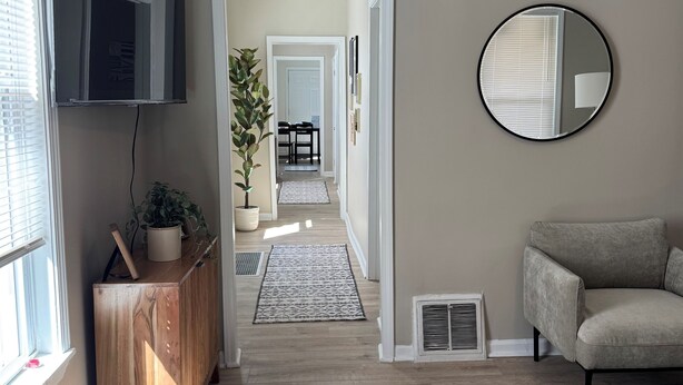 A hallway with a wooden cabinet, a potted plant, a round mirror, and a grey sofa. - La Casetta Cafe on The Hill (St. Louis)