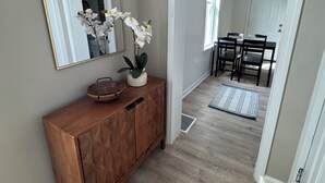 A hallway with a wooden cabinet, a mirror, white orchids, a small bowl, and a dining area with chairs and a table. - La Casetta Cafe on The Hill (St. Louis)