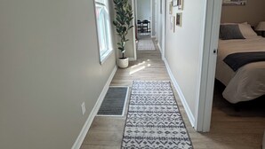 A narrow hallway with a potted plant, patterned rugs, a bed with a blanket, and framed pictures on the wall. - La Casetta Cafe on The Hill (St. Louis)