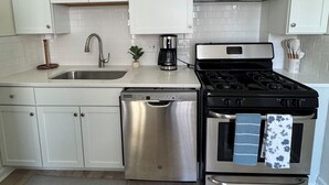 A modern kitchen with white cabinets, stainless steel appliances, a microwave, and a gas stove. - La Casetta Cafe on The Hill (St. Louis)