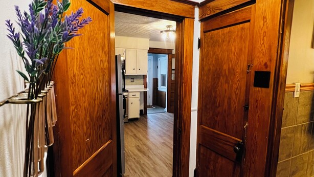 A hallway with wooden doors, a kitchen area visible through an open door, and a vase with purple flowers on the left. - Casa Italiana: Cozy home in the heart of The Hill (St. Louis)