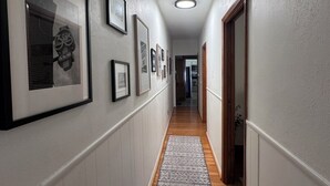 A hallway with framed pictures on the walls, a patterned rug, and a wooden floor. - Casa Italiana: Cozy home in the heart of The Hill (St. Louis)