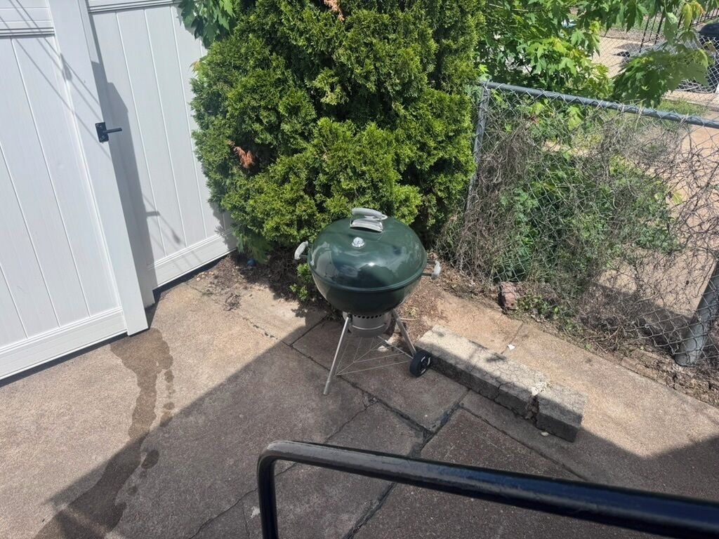 A barbecue grill outside a house with a white door and a metal fence.