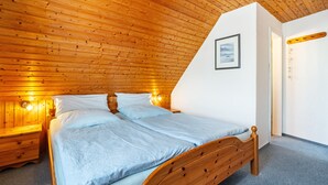 A bedroom with a wooden ceiling, a bed with a wooden headboard, a nightstand, and a wall-mounted shelf. - Apartment Barlach, 35 sqm, 1 Bedroom, Max. 2 Guests (Pellworm)