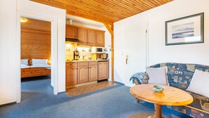 A cozy room with a wooden ceiling, a bed, a dining table, and a sofa. - Apartment Barlach, 35 sqm, 1 Bedroom, Max. 2 Guests (Pellworm)