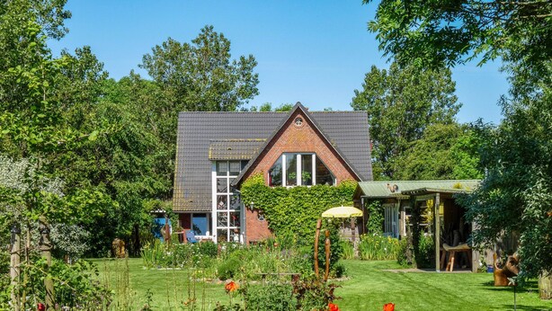 A house with a brick exterior, a sloped roof, and a large garden with various plants and flowers. - Apartment Nolde, 33 sqm, 1 Bedroom, Max. 2 Guests (Pellworm)