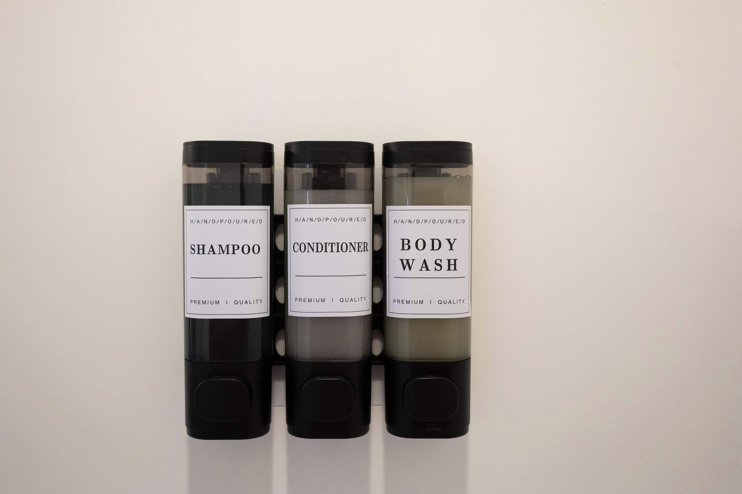 Drei Flaschen mit Haarpflegeprodukten, beschriftet mit Shampoo, Conditioner und Duschgel.