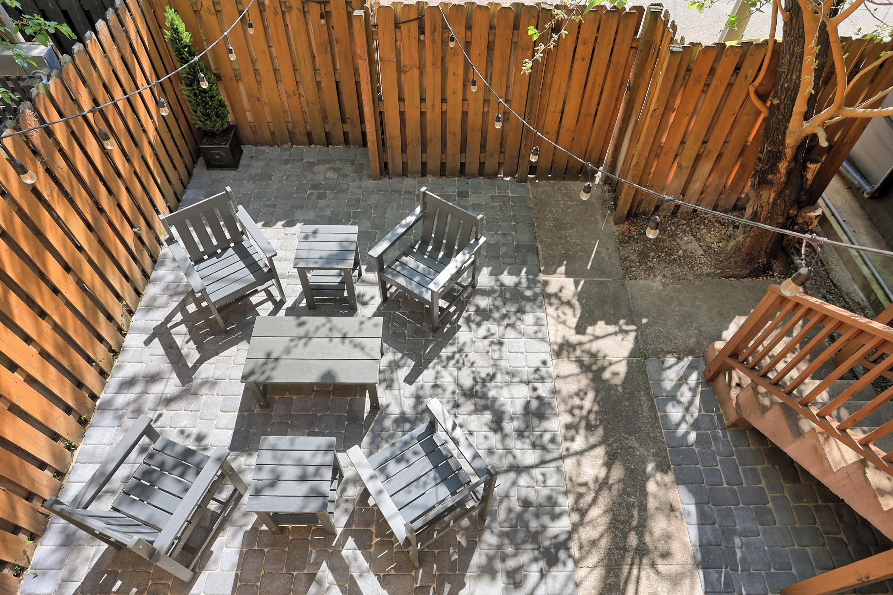 A patio area with a wooden fence, outdoor furniture, and string lights.
