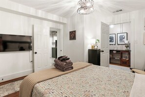 A bedroom with a bed, a TV, a door, and a cabinet. - Historic Garden-Level Downtown Apt with Backyard (Savannah)
