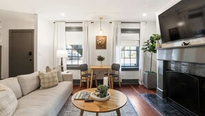 Una sala de estar con sofá, mesa de centro, chimenea, televisor y comedor con sillas y mesa.