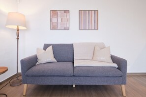 Un canapé gris avec deux coussins, un lampadaire et deux œuvres d’art encadrées accrochées au mur.