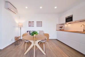 A modern kitchen with white cabinets, a wooden dining table, and a built-in oven. - Finca El Moral by Huskalia - Apartamento 1 (Los Llanos de Aridane)