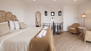 Une chambre d'hôtel dotée d'un grand lit, d'un coin salon avec des meubles en osier, et d'un escalier menant à un étage supérieur.