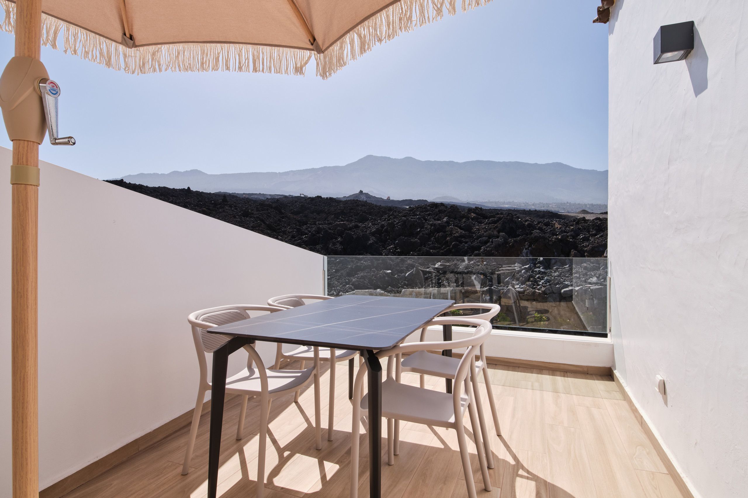 A balcony with a table and chairs, a view of a mountainous landscape, and a clear sky.