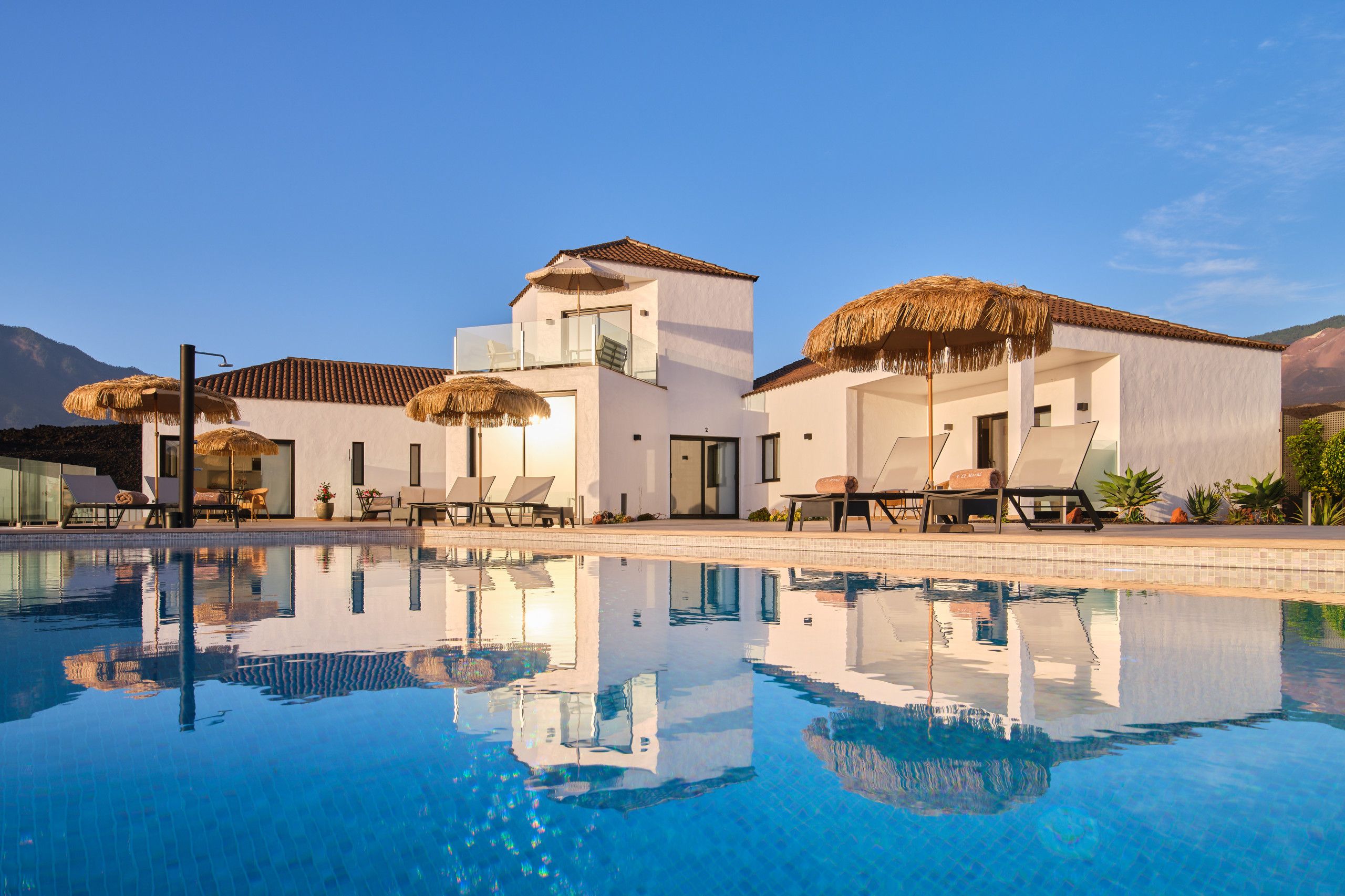 Ein modernes Resort mit Pool, Liegestühlen und Reetdachschirmen.