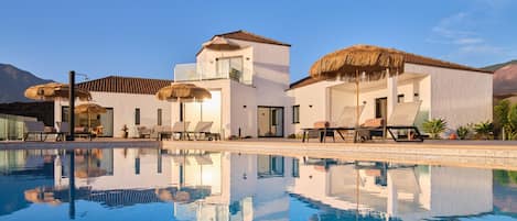 A modern resort with a clear pool, sun loungers, and thatched umbrellas.