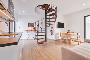 Eine moderne Küche mit integriertem Backofen, ein Essbereich mit rundem Tisch und Stühlen sowie eine Wendeltreppe.
