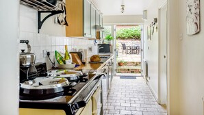 A narrow kitchen with a stove, cabinets, and a dining area visible through an open door. - Rose Cottage - sleeps 4 guests  in 2 bedrooms (Burnham Market)
