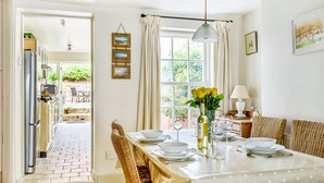 A dining area with a table set for four, a chandelier, and a view of the garden through the window. - Rose Cottage - sleeps 4 guests  in 2 bedrooms (Burnham Market)