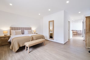 Ein modernes Schlafzimmer mit einem großen Bett, Nachttischlampen, einer Bank und einem Spiegel.