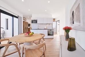 Eine moderne Küche mit weißen Schränken, einem eingebauten Ofen und einem Essbereich mit Holztisch und -stühlen.