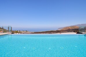 Ein klares, blaues Schwimmbecken mit Blick auf den Ozean und die dahinter liegenden Hügel.