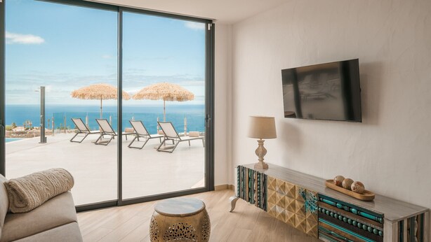 Un salón moderno con un amplio ventanal corredera que da a un balcón con sillones de descanso y vistas al mar.