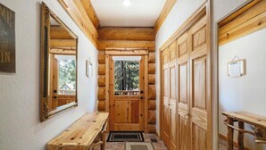 Interior de uma cabana de tronco com um banco de madeira, uma porta para o exterior e um espelho na parede.