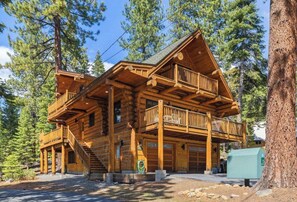 Une cabane en rondins à plusieurs étages, dotée d’un balcon et entourée d’arbres.