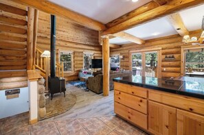 A log cabin interior with a fireplace, wooden furniture, and a large window overlooking the outdoors. - Mashie Meadows log home hot tub boot dryer sleeps 10 + 2 close to skiing & beach (Tahoe Vista)