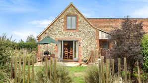 Una casa de piedra con techo de tejas, una valla de madera y un patio con mobiliario exterior.