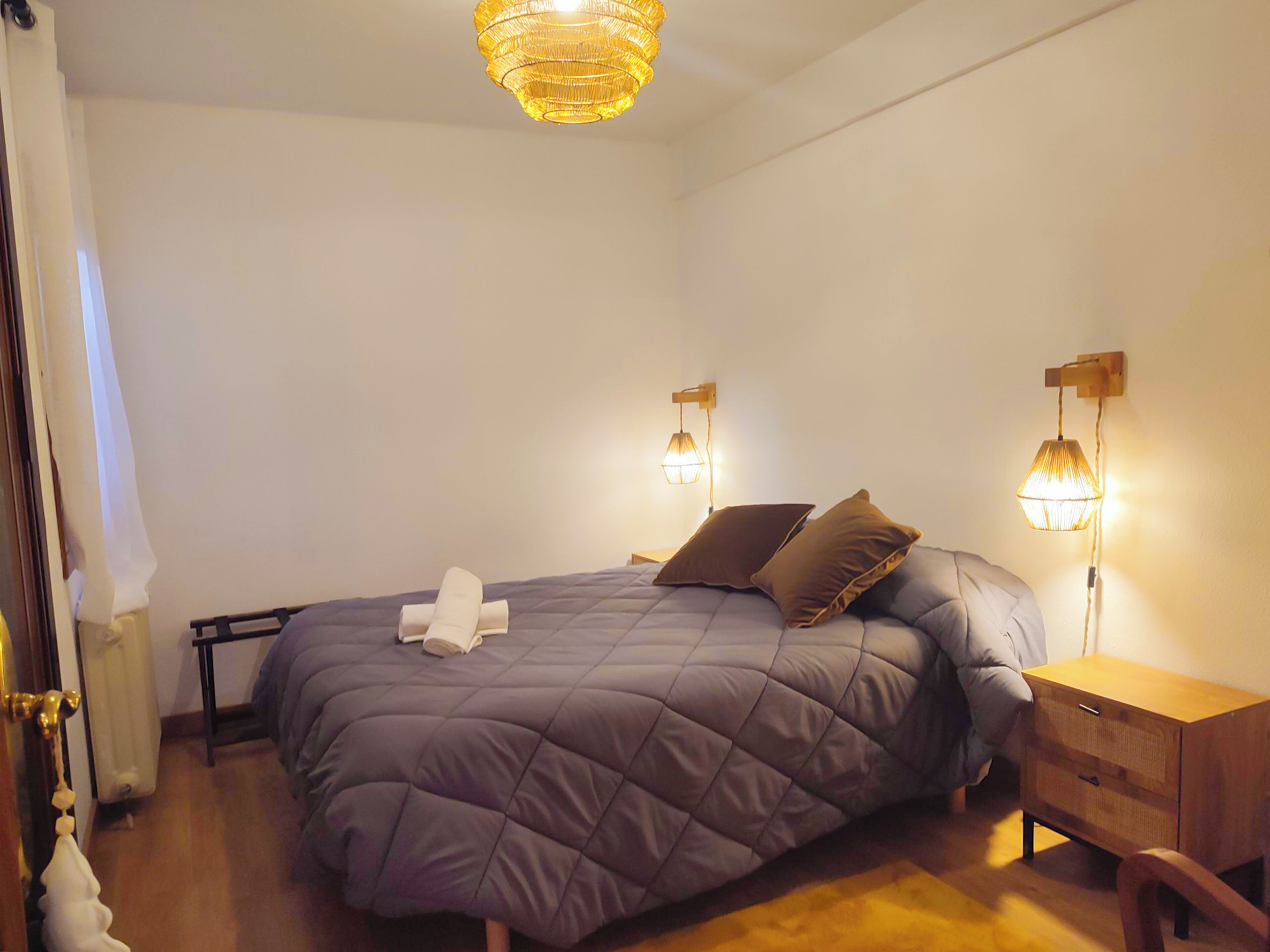 A bedroom with a large bed, two bedside tables, a wooden dresser, and a hanging light fixture.